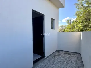 Fachada branca de uma residência com porta de entrada aberta para um pátio.