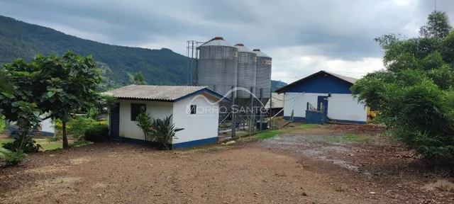 Vista externa de uma propriedade rural com estruturas simples e silos ao fundo.