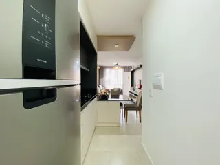 Vista de um corredor que conecta a cozinha a uma sala de jantar iluminada.