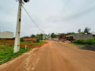 Uma estrada de terra vermelha se estende por uma área com construções ao fundo.