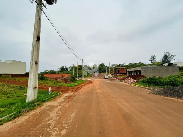 Uma estrada de terra vermelha se estende por uma área com construções ao fundo.