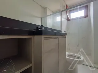 Banheiro com bancada escura e box de vidro transparente.