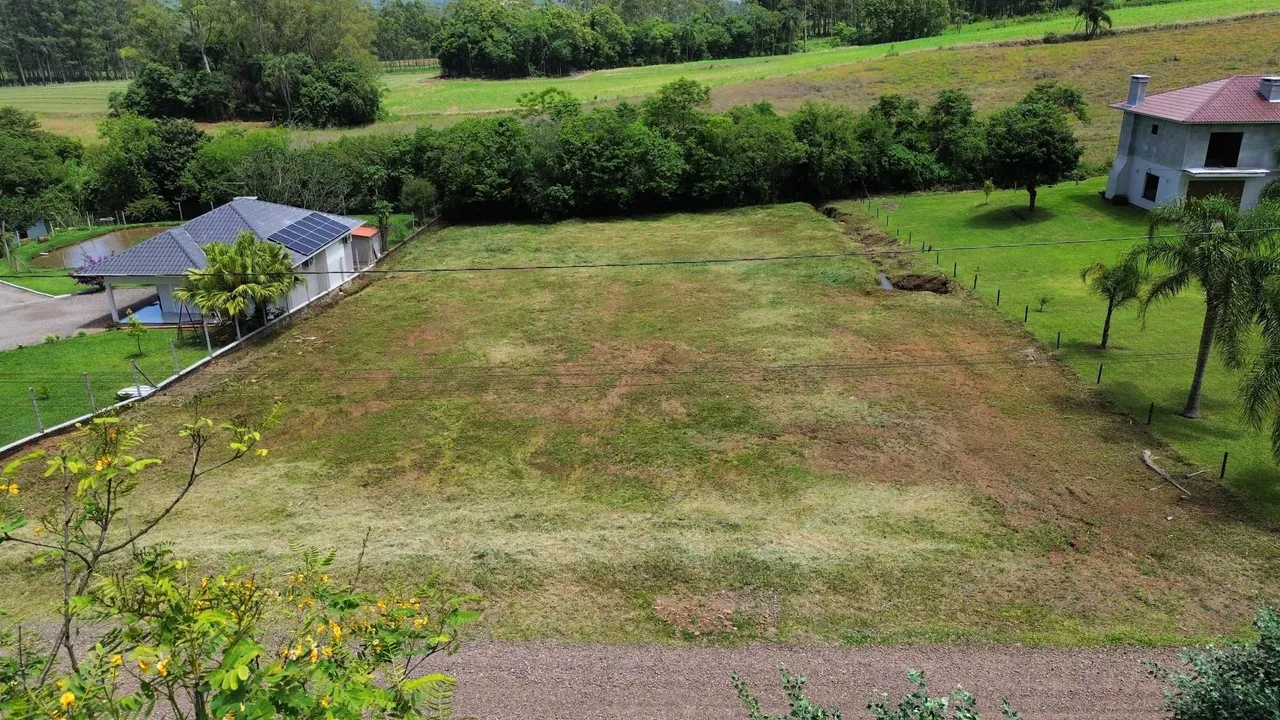 Vista externa de um terreno gramado com vegetação ao fundo.