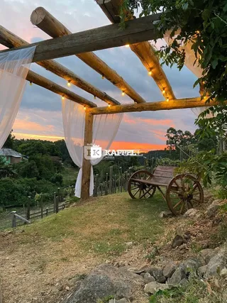 Uma estrutura de madeira rústica com um céu ao pôr do sol é visível no jardim.