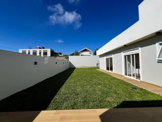 Fachada de uma residência branca com um jardim gramado e deck de madeira.