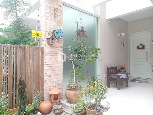 Vista da fachada de uma residência com muro de tijolos e jardim.