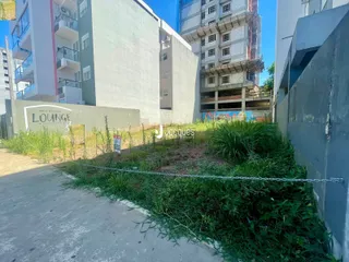 Vista externa de um terreno com vegetação densa entre edifícios residenciais.