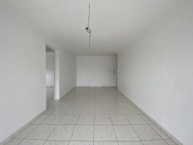 Corredor longo com piso de azulejos claros e paredes brancas.