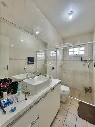 Banheiro com revestimento cerâmico branco e box de vidro.