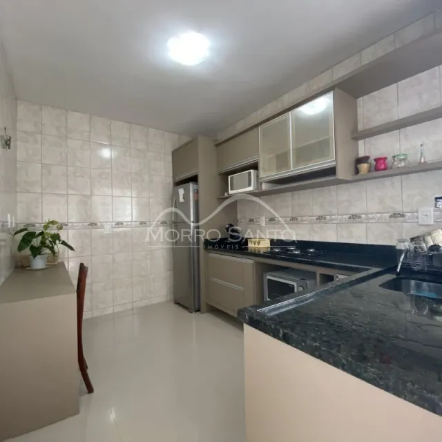 Cozinha com revestimento de azulejos brancos e bancada escura.