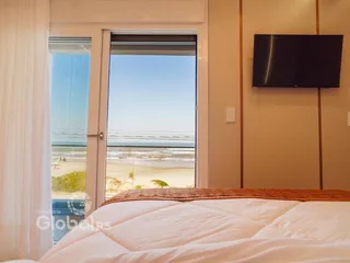 Quarto com vista para o mar através de uma porta de vidro.