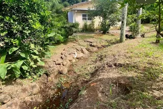 Paisagem de terreno seco com vegetação e um leito de riacho na propriedade.
