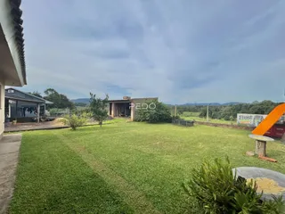 Vista externa de um terreno gramado com uma casa ao fundo.