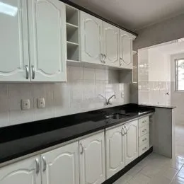 Cozinha com armários brancos e bancada escura.