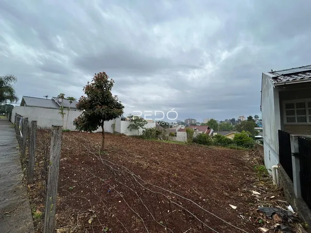Vista da propriedade com terreno inclinado e vegetação ao longo da cerca.