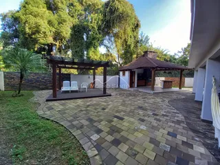 Área externa pavimentada com pedras e um pergolado de madeira é visível na propriedade.