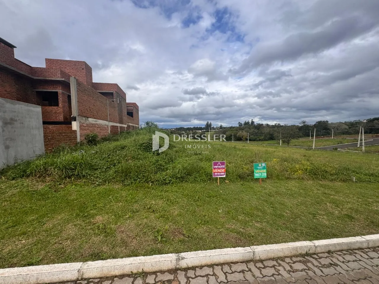 Vista externa de uma propriedade com gramado e construção de tijolos vermelhos.