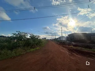Uma estrada de terra se estende por uma paisagem com vegetação e construções ao fundo.
