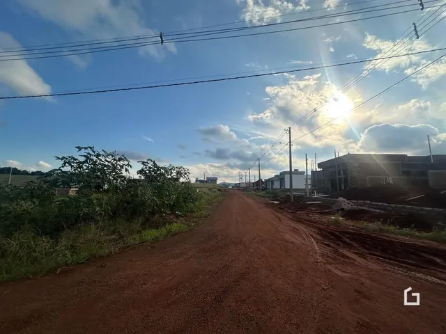 Uma estrada de terra se estende por uma paisagem com vegetação e construções ao fundo.