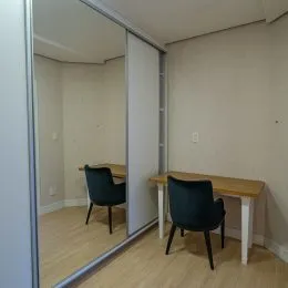 Vista interna de um cômodo com piso de madeira clara e paredes brancas.