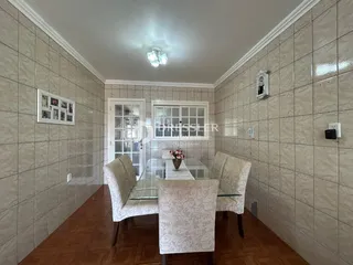 Uma sala de jantar com mesa de vidro e cadeiras estofadas em um imóvel no Brasil.