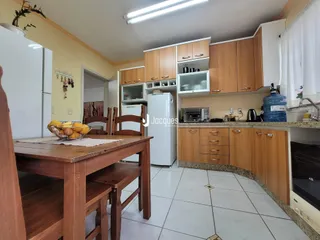 Vista interna de uma cozinha e sala de jantar com armários de madeira e piso cerâmico.