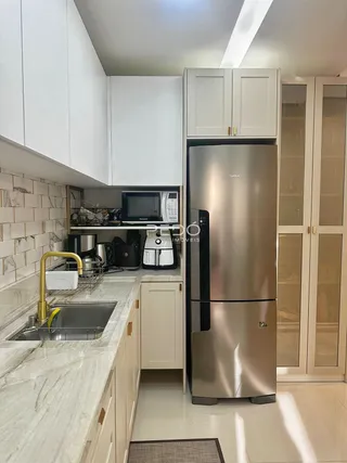 Vista da cozinha com armários brancos e bancadas de mármore claro.