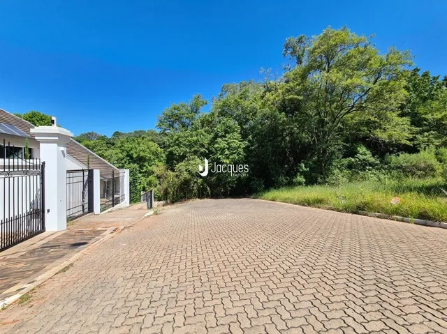 Vista externa de uma área pavimentada com árvores ao fundo.