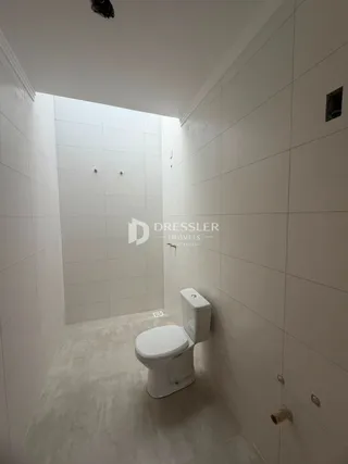 Corredor interno com revestimento branco e vaso sanitário.