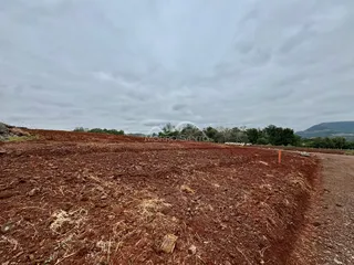 Vista de terra vermelha e seca com vegetação rasteira em um terreno aberto.