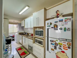 Vista interna de uma cozinha moderna com armários brancos e eletrodomésticos.