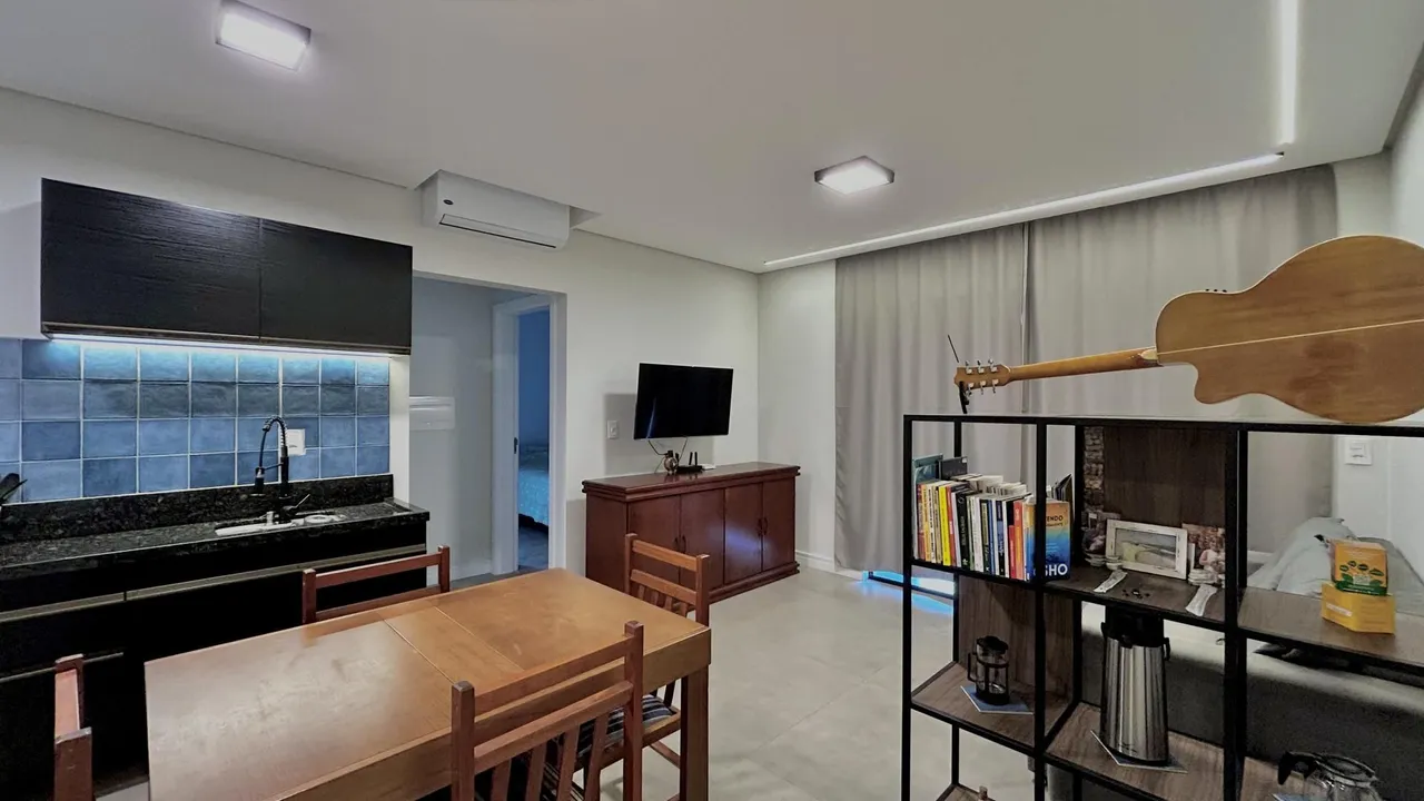 Ambiente interno com mesa de jantar de madeira e estante decorativa em um apartamento.