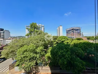 Vista aérea de uma área residencial com vegetação densa e edifícios ao fundo.