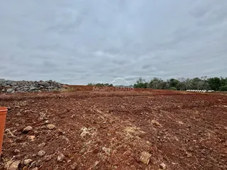 Vista de uma área de terra vermelha e seca com vegetação rasteira no fundo.