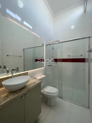 Banheiro com box de vidro e pia de apoio em cerâmica.
