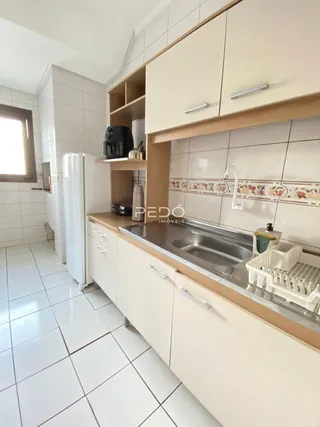 Vista interna de uma cozinha com armários brancos e piso de cerâmica.