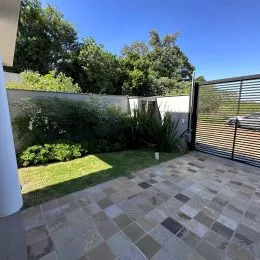 Área externa pavimentada com lajotas e vegetação ao fundo.