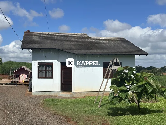 Fachada de uma casa branca com telhado escuro em uma área rural.