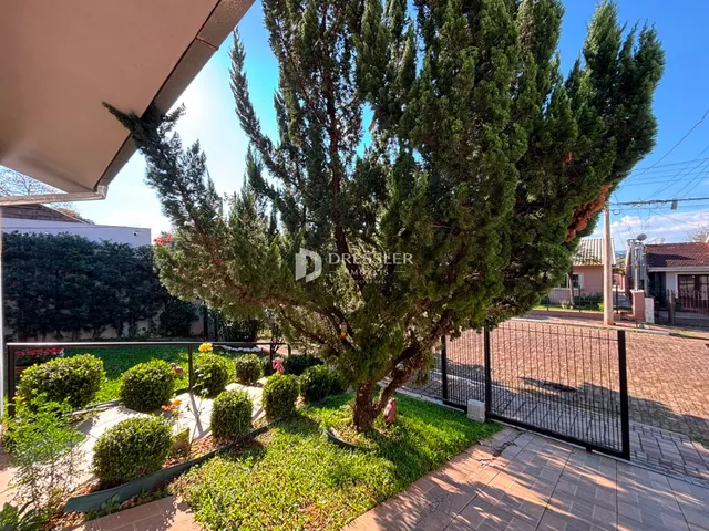 Vista externa de um jardim com árvores e cerca em uma propriedade residencial.