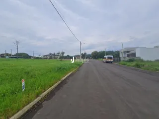 Vista de uma estrada rural com campo gramado e uma edificação ao fundo.