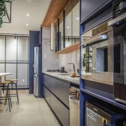 Foto interna de uma cozinha moderna com armários escuros e bancadas claras.