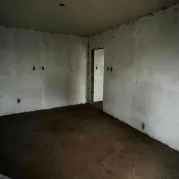 Foto interna de um cômodo com paredes brancas e piso cru.