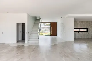 Hall de entrada amplo com piso de porcelanato claro e escadaria de vidro.