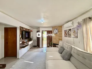 Sala de estar com sofá branco e televisão em ambiente claro.