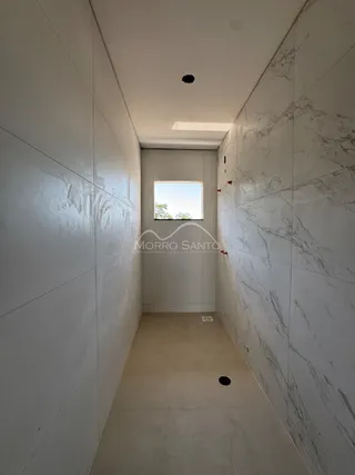 Corredor longo com paredes brancas e uma porta no final, mostrando o interior de uma residência.