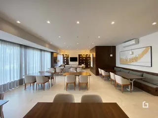 Sala de estar ampla com piso claro e grandes janelas.