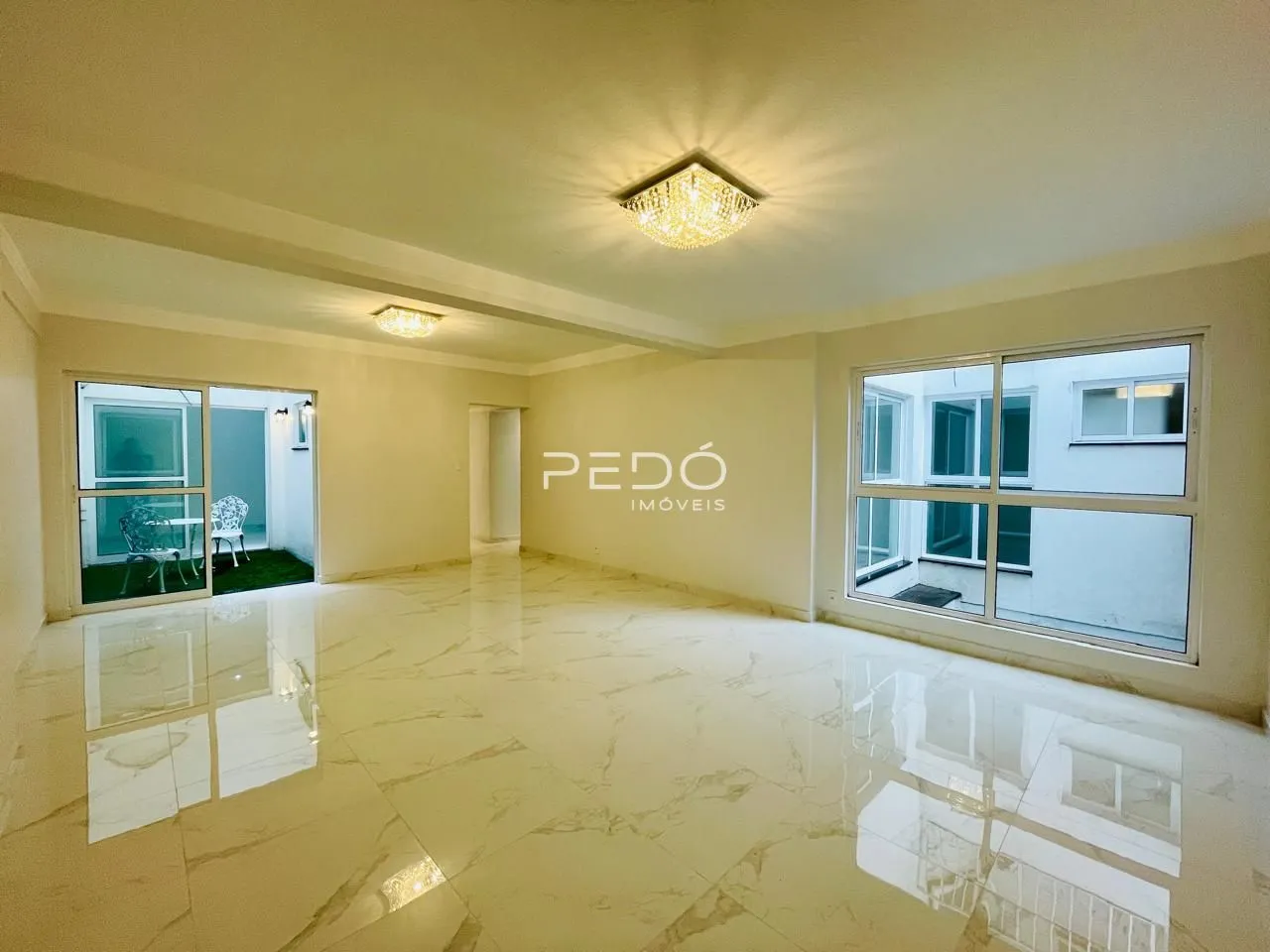 Ambiente interno amplo com piso de mármore claro e grandes janelas.