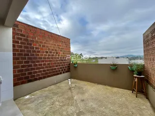 Vista externa de um pátio com parede de tijolos aparentes e piso de concreto.