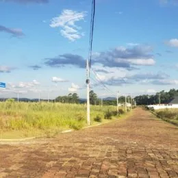 Vista externa de um caminho de terra em uma área gramada sob um céu azul.