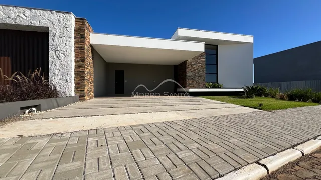 Fachada externa de uma casa moderna com revestimento de pedra e área de acesso pavimentada.